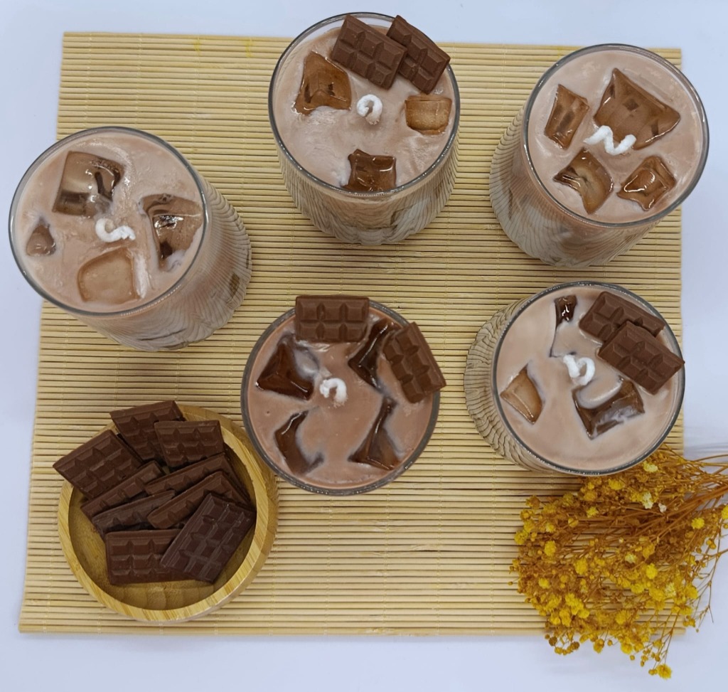 Beş adet iced mocha mumunun bambu hasır üzerinde üstten çekimi; buz küpü efektleri, fitiller ve ahşap kâsede çikolata tabletleri