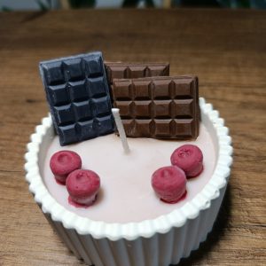 Kırmızı meyveli ve çikolatalı el yapımı soya mumu: oluklu kapta pembe mum, üzerinde ahududu figürleri ile bitter ve sütlü çikolata tabletleri